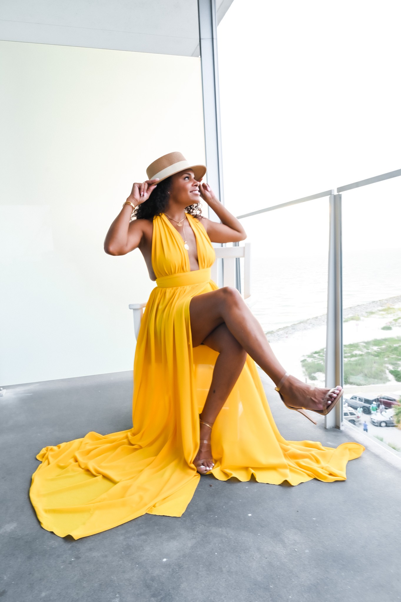 Tiff LaQueen sitting on balcony with yellow dress and white hat